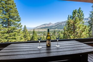 A wooden table with a bottle of wine and two glasses on a balcony overlooking a mountainous landscape. - Ski-In/Ski Out | Hot Tub | Mountain Views (Mammoth Lakes)