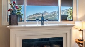 Une cheminée donnant sur les montagnes, un vase rempli de fleurs et deux verres à vin posés sur le manteau de la cheminée.