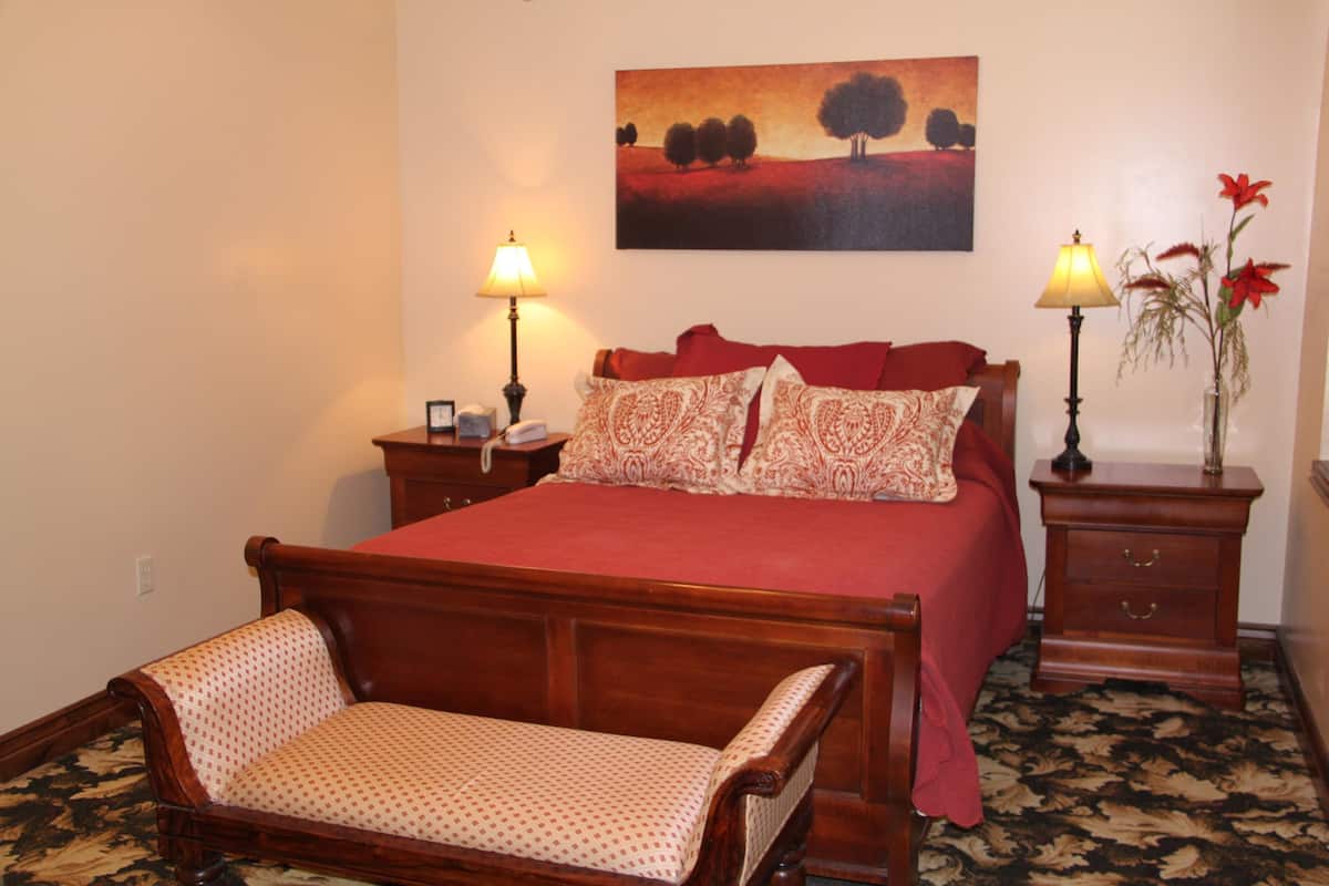 Quarto com cama de madeira, duas luminárias de cabeceira, mesa de cabeceira, um banco e um quadro na parede.