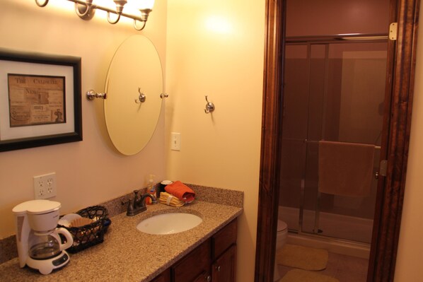 A bathroom with a sink, mirror, framed newspaper, coffee maker, and shower.