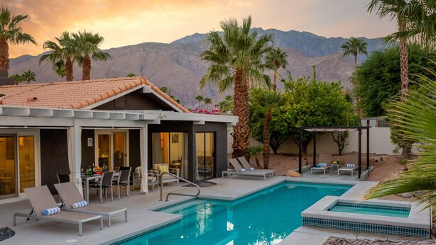 A pool area with lounge chairs, a dining table, and a view of mountains.