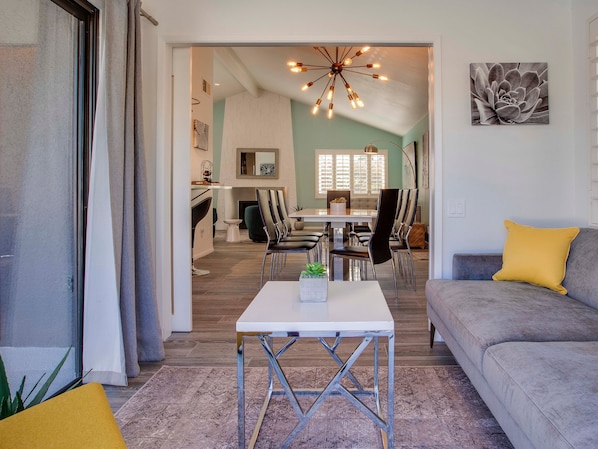 Un salon moderne avec un canapé, un coin repas comprenant des chaises et une table, et une cuisine en arrière-plan.