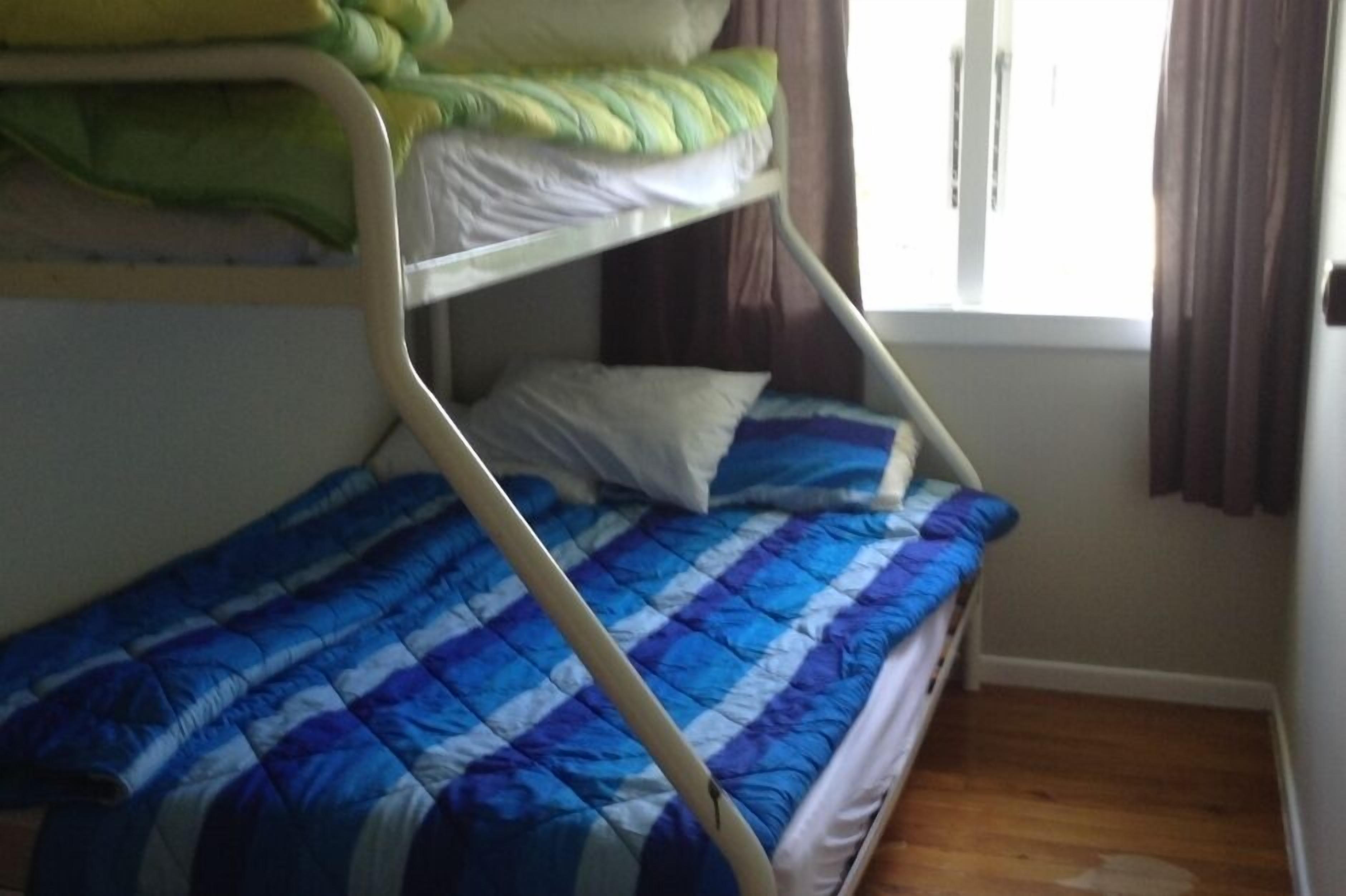 A bunk bed with a blue checkered bedspread and a green pillow on the top bunk.