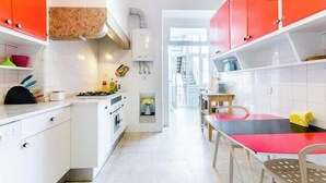 Une cuisine avec des meubles blancs, un fourneau et un coin repas comprenant une table et des chaises rouges.