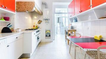 Une cuisine avec des meubles blancs, un fourneau et un coin repas comprenant une table et des chaises rouges.