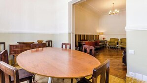 Un grand espace dédié à la salle à manger, avec une grande table et des chaises en bois, un petit coin cuisine équipé d’une cuisinière et de quelques sièges, et un salon avec un canapé et des fauteuils.