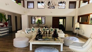 Ein geräumiges Wohnzimmer mit einer großen Couchgarnitur, einem Couchtisch und einem weißen Sessel. Übertöpfe und ein Kronleuchter sind ebenfalls vorhanden.