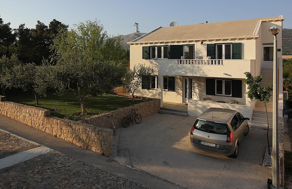 Una casa de dos pisos con un coche estacionado en la entrada, un muro de piedra y una bicicleta apoyada contra el muro.