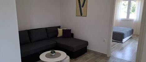A modern living room with a dark sectional sofa, a small round table, and a painting on the wall.