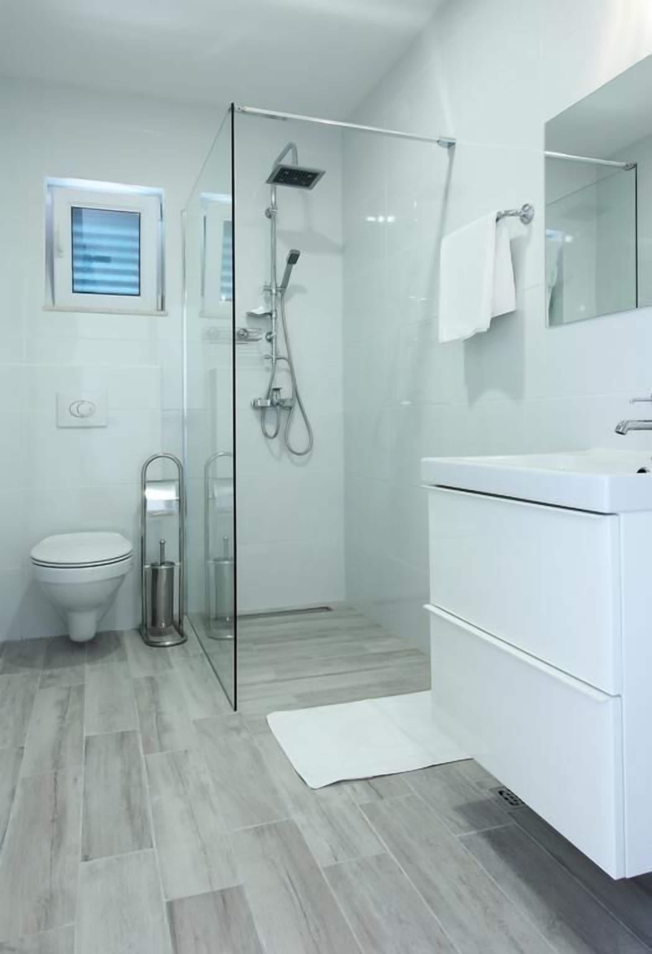 Un baño moderno con ducha de vidrio, inodoro y lavamanos blanco.