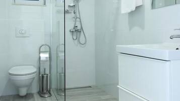 Un baño moderno con ducha de vidrio, inodoro y lavamanos blanco.
