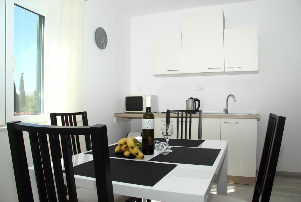 A modern kitchen with white cabinets, a microwave, and a sink. There is a dining table with chairs, a clock on the wall, and a window with a view of trees.