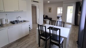 A modern kitchen with white cabinets, a dining area with a white table and black chairs, and a visible air conditioning unit. - Mocici apartments (Konavle)