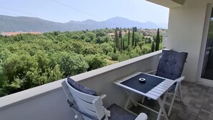 A balcony with two white chairs and a small table, overlooking a lush green landscape with mountains in the distance. - Mocici apartments (Konavle)