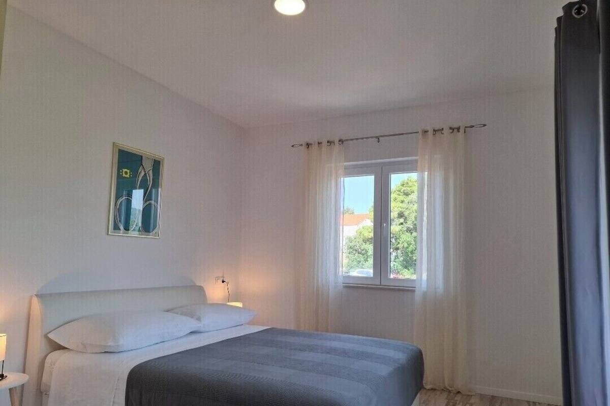 Une chambre à coucher avec un lit, une table de chevet avec une lampe, une fenêtre avec des rideaux et un tableau accroché au mur.