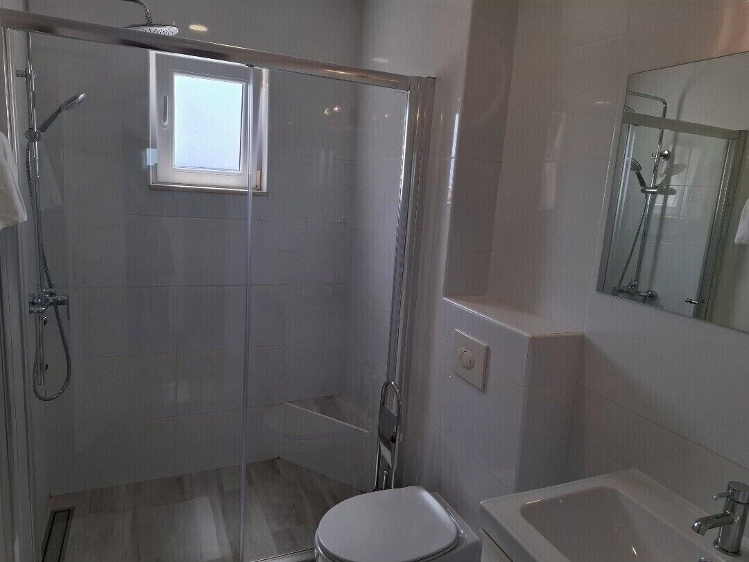 Une salle de bain moderne dotée d’une douche à parois de verre, de toilettes et d’un lavabo.