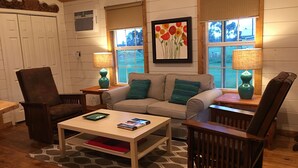 A cozy living room with a beige sofa, two armchairs, a coffee table, and a fireplace. There are two windows with blinds, a painting above the sofa, and a lamp on each side of the sofa. - Leroy's  farmhouse 7 min to Memphis, ❤️1 pet free 2nd pet considered for fee (Mound City)