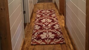 A narrow hallway with wooden walls and a patterned rug leading to a bedroom with a bed and a nightstand. - Leroy's  farmhouse 7 min to Memphis, ❤️1 pet free 2nd pet considered for fee (Mound City)