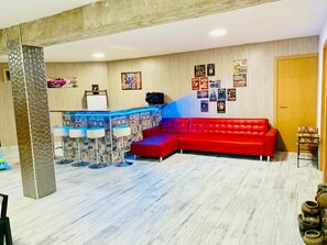 Ein modernes Wohnzimmer mit einem roten Modulsofa, einer Bar mit Hockern und einer Wand, die mit verschiedenen Postern dekoriert ist.