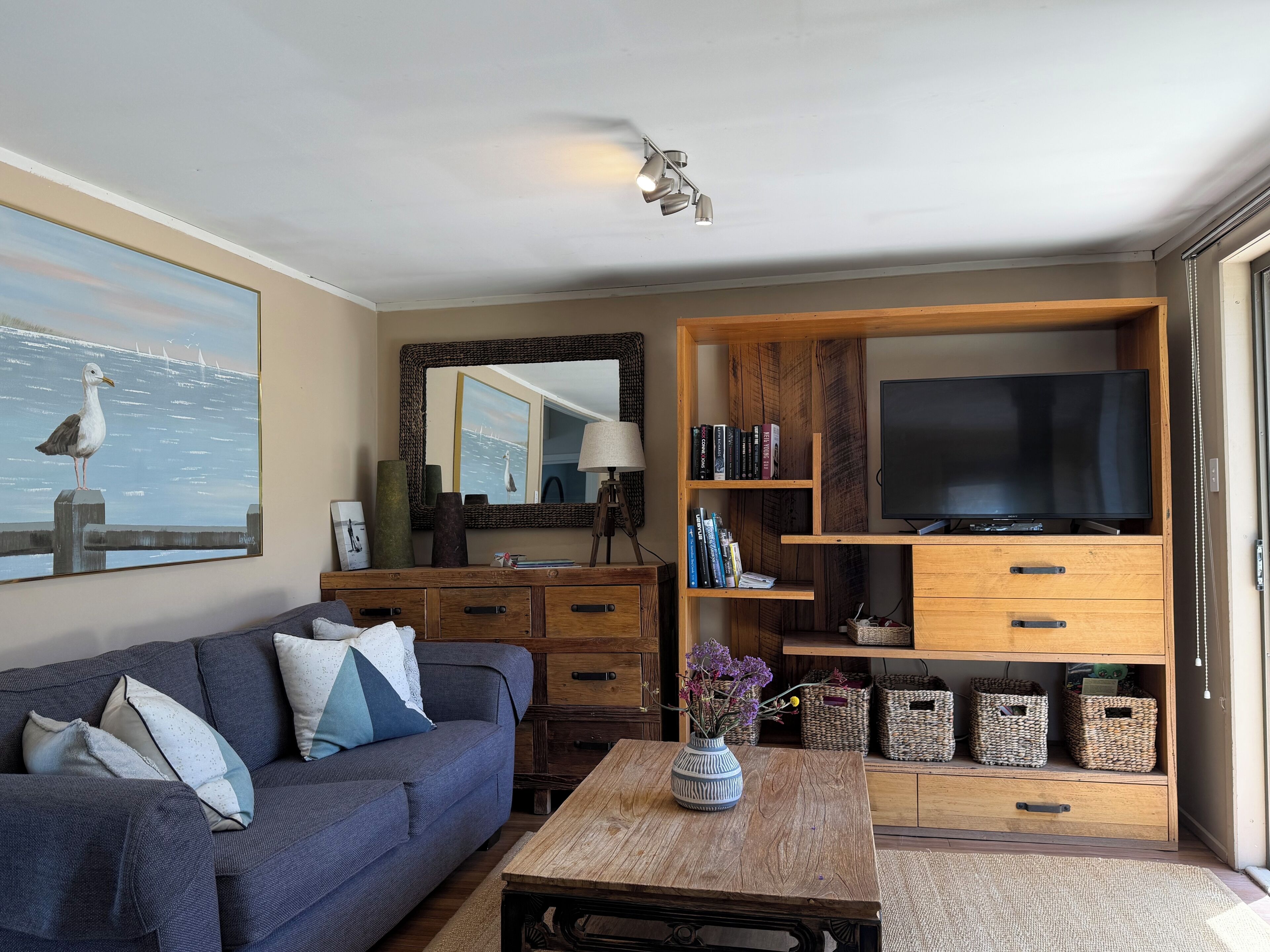A living room with a sofa, coffee table, TV stand, and shelves with books and decorative items.