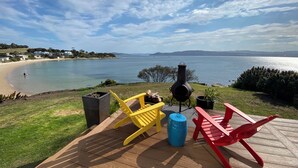 Eine Terrasse mit Sitzgelegenheit, Grill und Blick auf See und Strand.