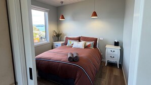 Ein Schlafzimmer mit Bett, Nachttischen, einem Fenster und Meerblick.