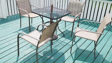 Relax on the deck with a metal table and four chairs, surrounded by lush greenery.