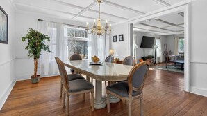 Een eetkamer met een grote tafel, stoelen, een kroonluchter en een potplant.
