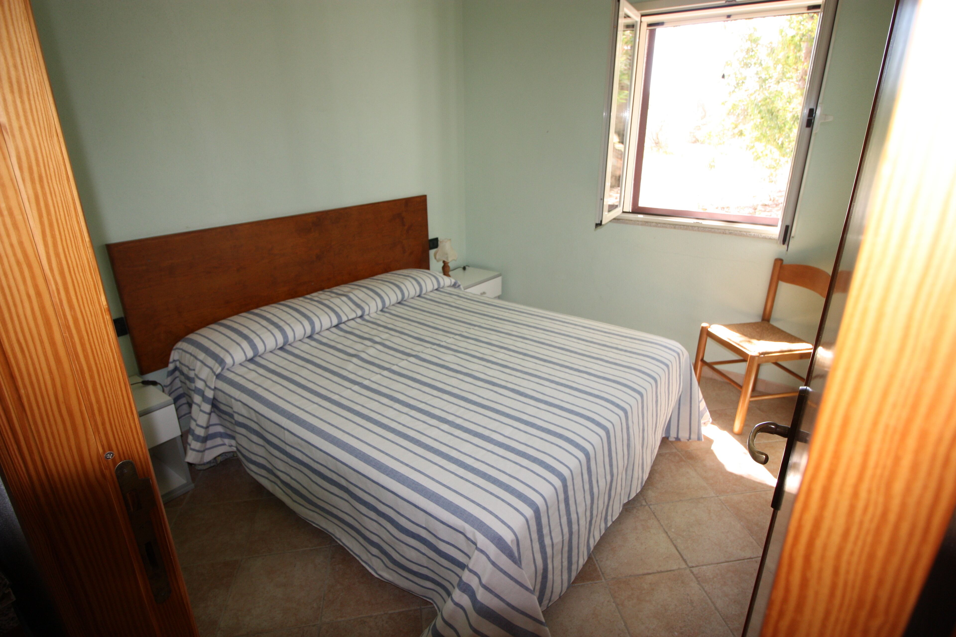 A bedroom with a bed, a nightstand, a chair, and a window.