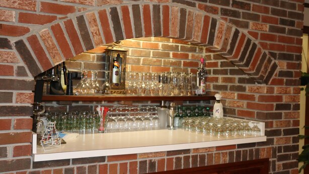 A bar area with a brick wall, shelves with glasses and bottles, and a white countertop.