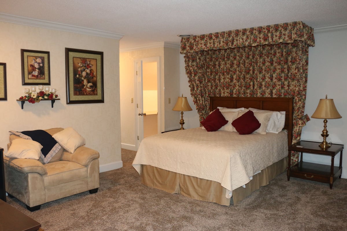 A bedroom with a bed, a chair, a nightstand, and a door.