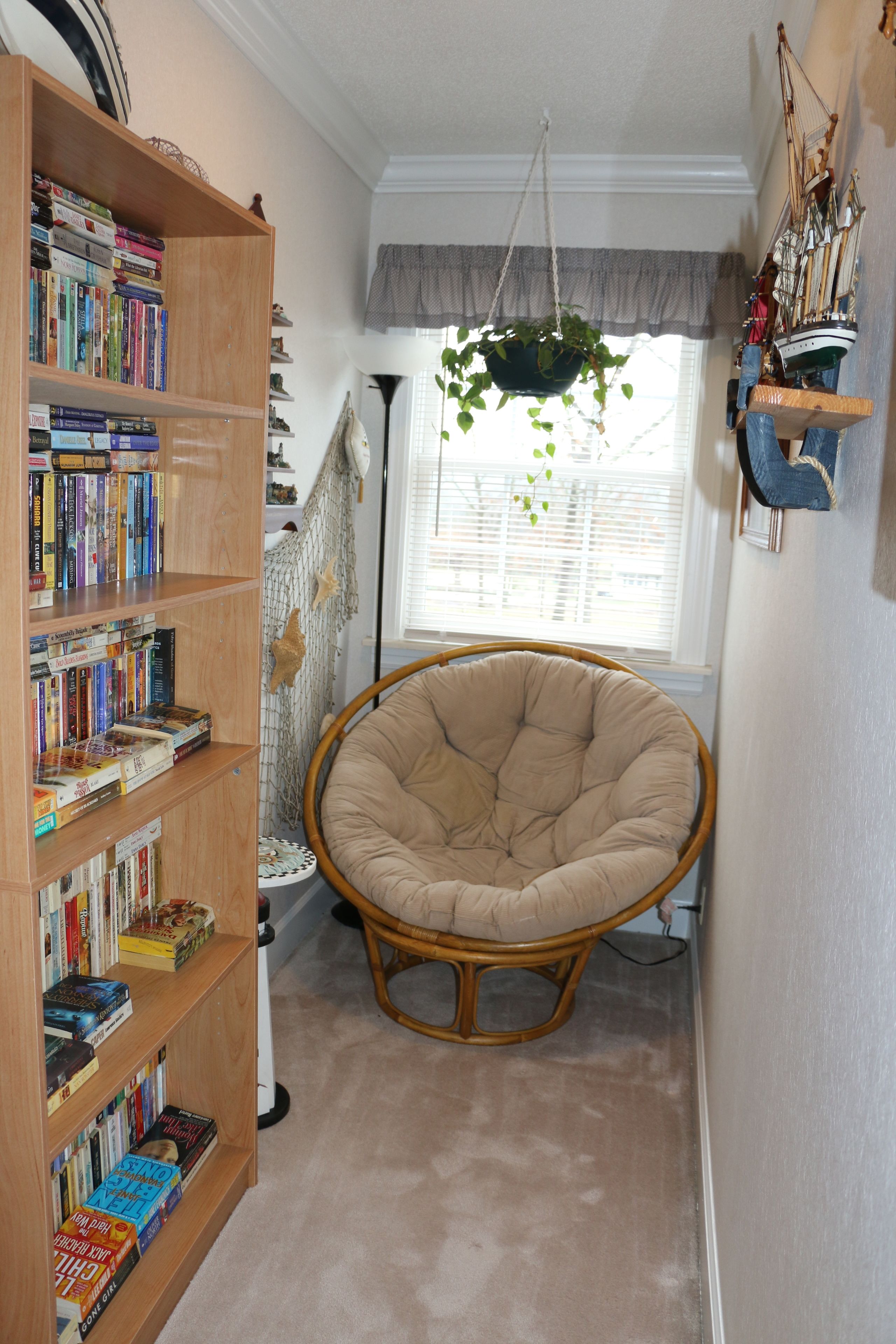 Een gezellige leeshoek met een grote boekenkast, een hangplant en een comfortabele fauteuil.