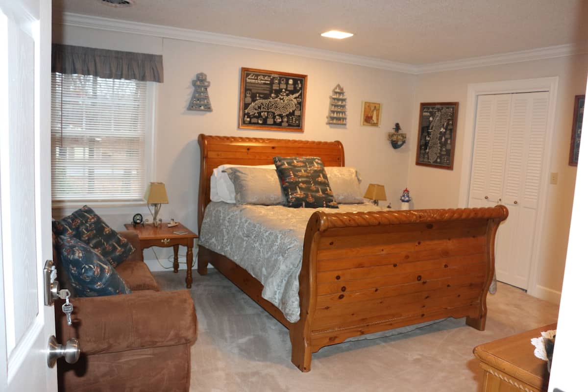 A bedroom with a wooden bed, a brown sofa, and a small table with a lamp.