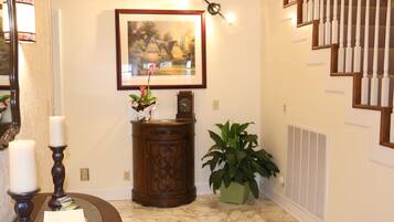 A hallway with a framed painting, a wooden cabinet, a potted plant, a mirror, and a staircase.