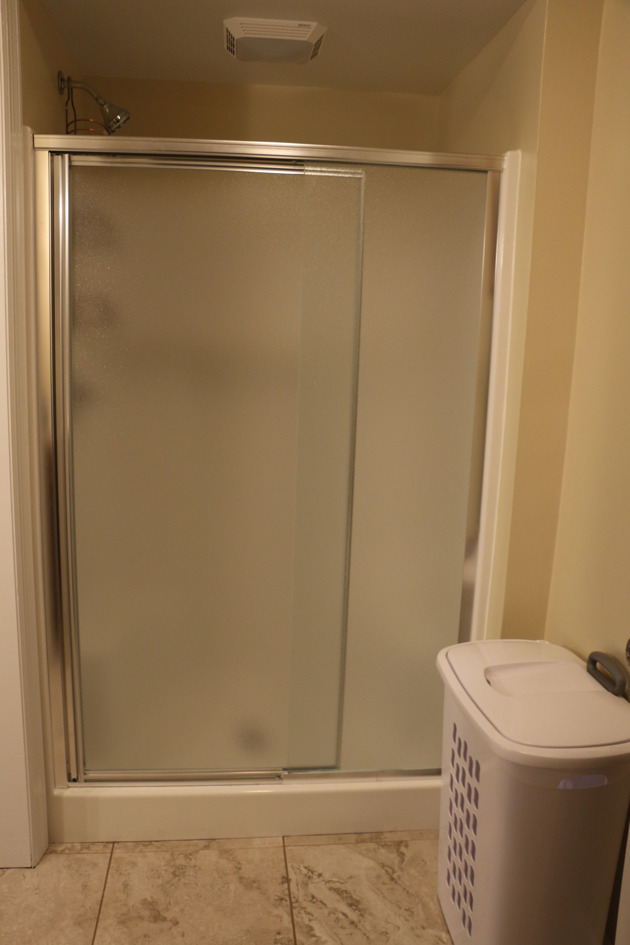 Un baño con cabina de ducha, inodoro y cesto de ropa.