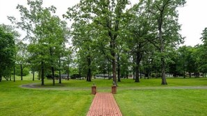 A paved pathway leading through a park with trees and a building in the background.