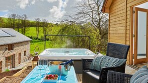 Ein Whirlpool mit Tisch für zwei Personen, ein Korbstuhl und ein Steinhaus im Hintergrund.