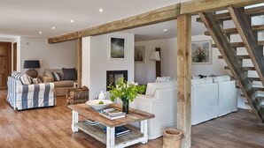 Ein großzügiger Wohnbereich mit Holztreppe, Kamin und weißem Sofa.