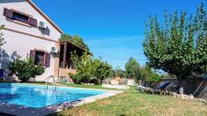 Une piscine à l’eau d’un bleu limpide, entourée d’une pelouse verdoyante et d’un bâtiment équipé de climatiseurs.