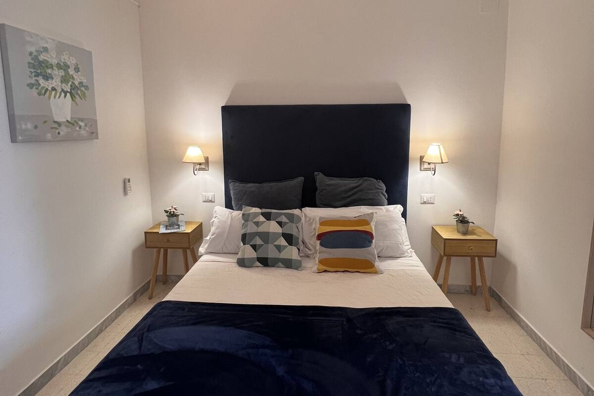 A neatly arranged bedroom with a large bed, two bedside tables, and a wall-mounted lamp.