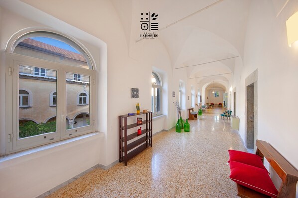 A hotel corridor with arched ceilings, a wooden bench with red cushions, and a small table with decorative items.