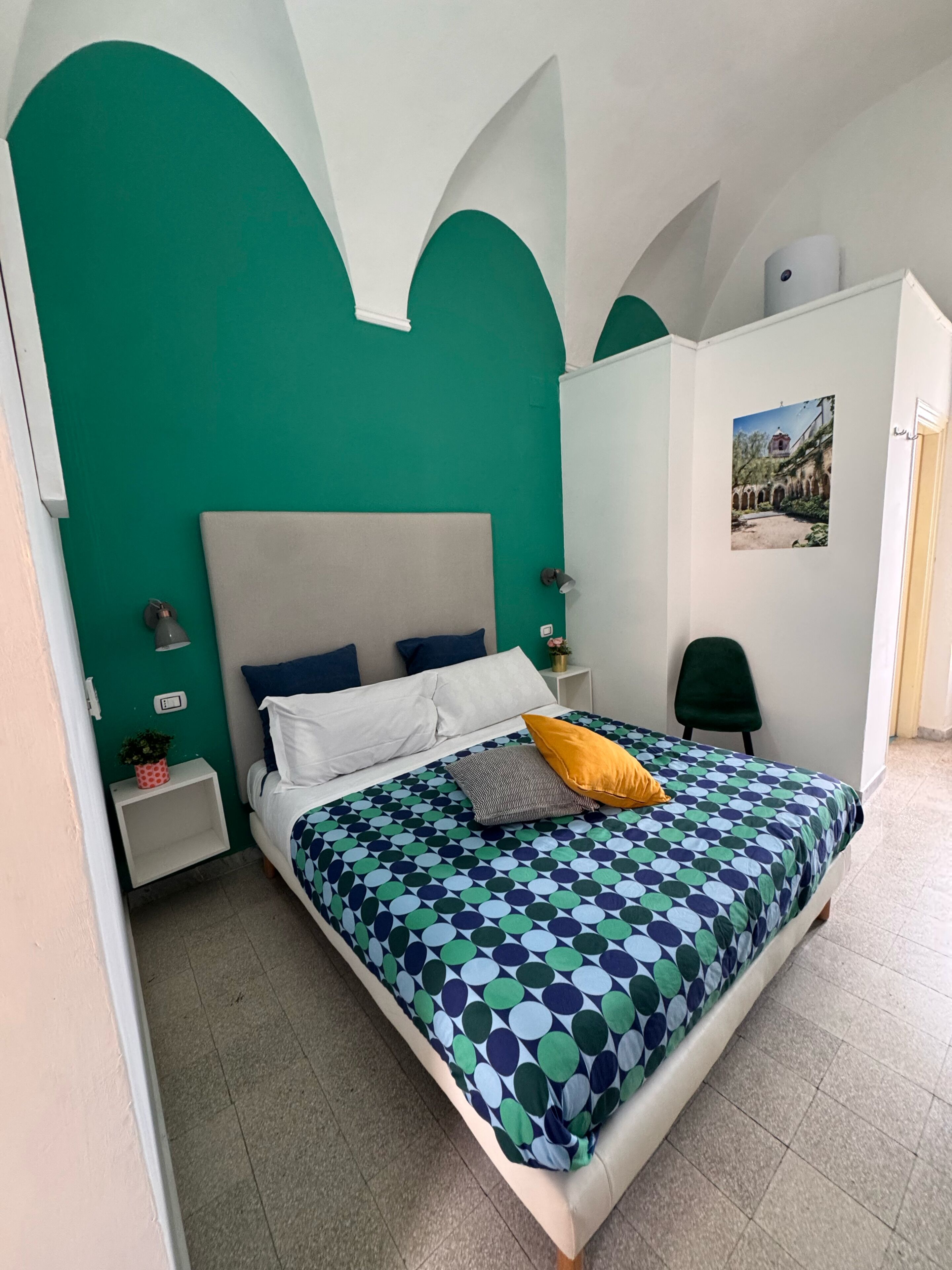 A bedroom with a bed, a nightstand, a green wall, a white wardrobe, and a picture on the wall.
