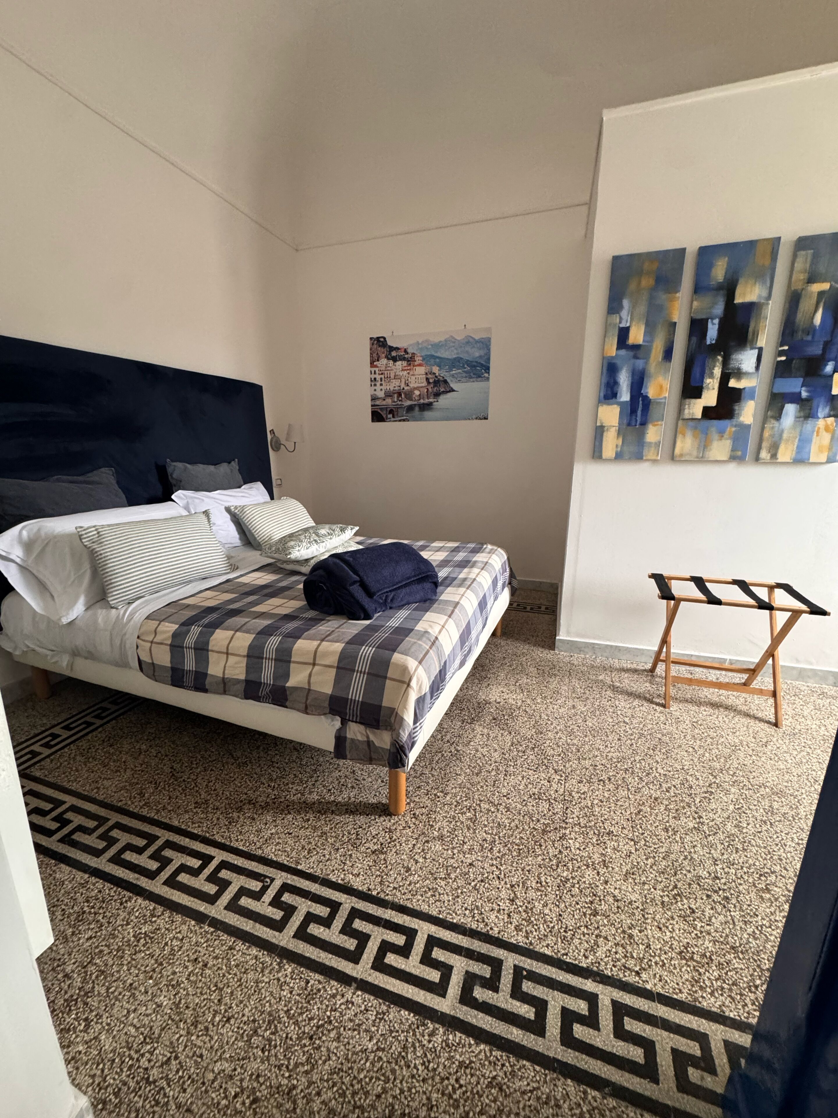 Ein Schlafzimmer mit Bett, Kopfteil, einem an der Wand befestigten Kunstwerk, einem kleinen Holzschemel und einem gemusterten Teppich.