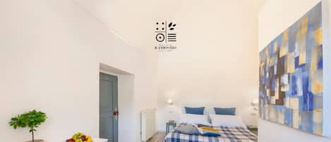 A modern bedroom with a bed, bedside table, chair, and a wall-mounted artwork.
