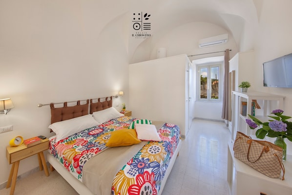 A bedroom with a bed, bedside tables, a TV, and a view to the outside.