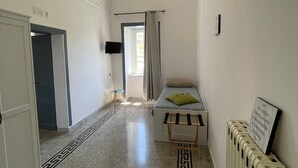 A narrow hallway with a bed, a radiator, and a television on the wall. - Relais il Chiostro Historic Courtyard and Panoramic Terrace near Sorrento (Massa Lubrense)