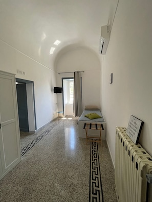 A narrow hallway with a bed, a radiator, and a television on the wall.