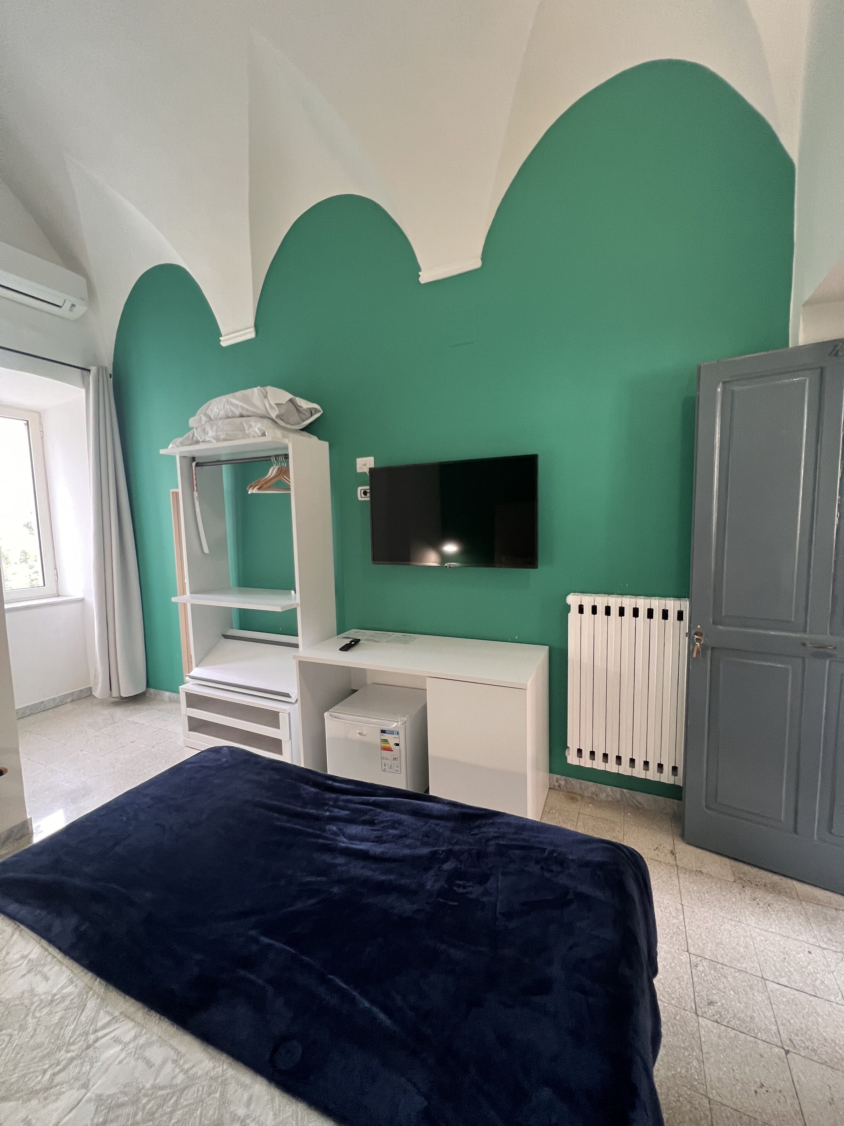 Un dormitorio con cama, escritorio, televisión, radiador y armario.