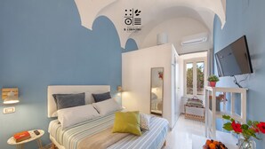 A bedroom with a bed, bedside table, and a small table with a book and remote control. - Relais il Chiostro Historic Courtyard and Panoramic Terrace near Sorrento (Massa Lubrense)