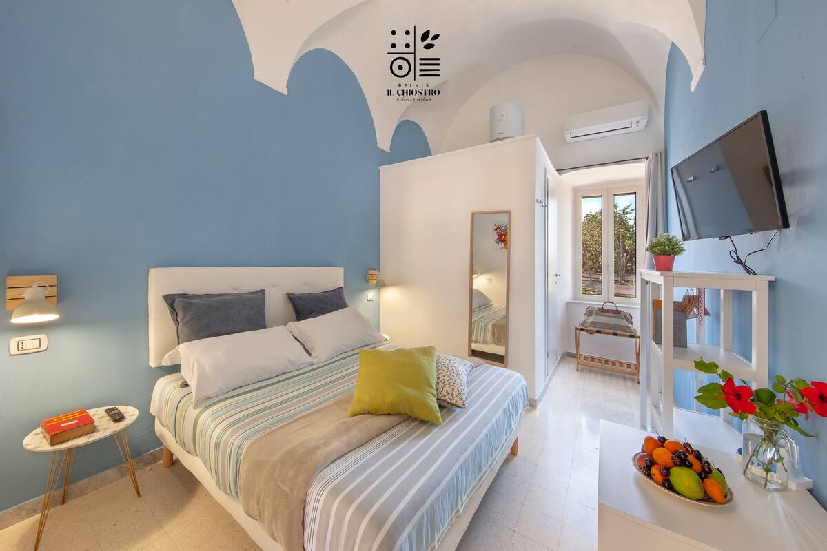 A bedroom with a bed, bedside table, and a small table with a book and remote control.